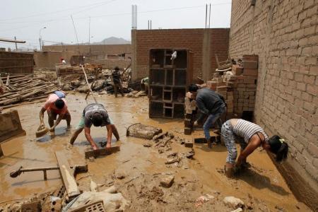 Gente remueve lodo de una casa tras un deslave e inundación en el barrio de Lurigancho en Chosica, Perú