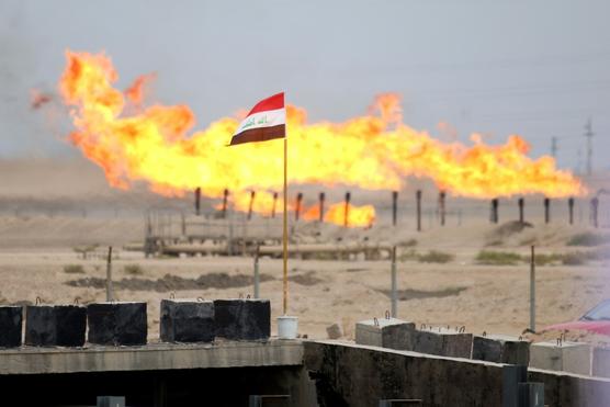 Bandera iraquí ondea frente a las llamas de la quema de un excedente de gas en un conducto de la refinería de petróleo de Zubair