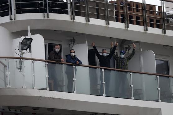 Los pasajeros del crucero australiano Greg Mortimer levantan los pulgares desde un balcón antes de desembarcar