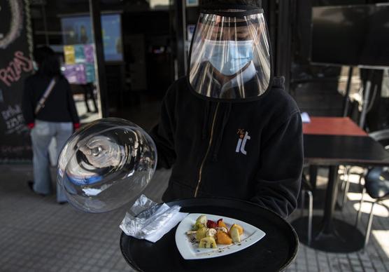 Un mesero, usando equipo de protección, muestra un plato de fruta durante la reapertura de un restaurante en Santiago