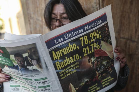 Una mujer lee un periódico que muestra los resultados del plebiscito del día anterior a favor de reescribir la Constitución