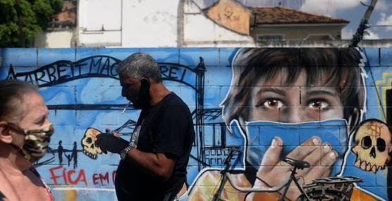 Personas con máscaras protectoras pasan junto a un graffiti, luego del brote de la enfermedad por coronavirus (COVID-19), en Río