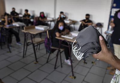 un maestro sostiene mascarillas para entregar a los estudiantes el primer día de regreso a la clase presencial