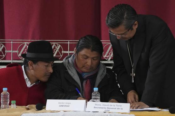 Los líderes indígenas Leonidas Iza, izquierda, y Marlon Vargas, al centro, firman un acuerdo junto a monseñor David de la Torr